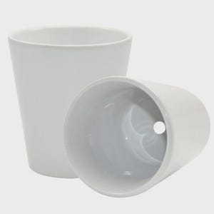 May include: Two white ceramic plant pots. One pot is upright, and the other is on its side. The pots have a smooth, glossy finish and a simple, modern design. The pots are suitable for indoor or outdoor use.