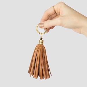 May include: A brown leather tassel keychain with a gold metal ring and a gold metal cap.