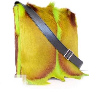 May include: A square-shaped, colorful handbag with a black shoulder strap. The bag is made of a textured material with a mix of yellow, brown, and green hues. The strap is made of black leather and has a silver-colored buckle.