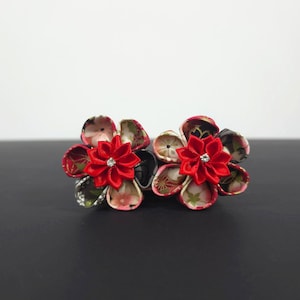 May include: Two fabric hair accessories featuring layered petals in floral patterns of pink, black, and white. Each flower is centered with a bright red, multi-petaled fabric element and a small, clear, sparkling crystal accent in the middle.
