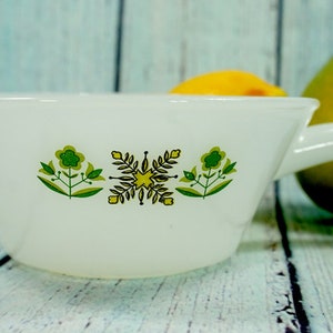 May include: White vintage teacup with a handle, decorated with green and yellow floral patterns. The teacup is set against a light blue background, with a pear and lemon in the background. A charming piece for tea lovers.