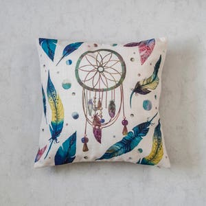 May include: A white pillow with a dreamcatcher design. The dreamcatcher is surrounded by colorful feathers and beads. The pillow is perfect for adding a bohemian touch to any room.