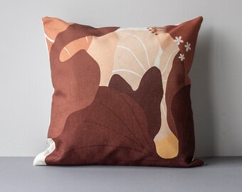 May include: A brown and beige throw pillow with a floral pattern. The pillow has a white background with brown and beige abstract shapes and white flowers.