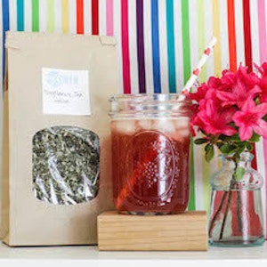 May include: A glass jar filled with iced tea, a brown paper bag with a label that reads "Sweet Leaf Tea", a pink flower in a glass vase, and a wooden block.