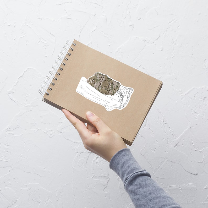 May include: A brown notebook with a spiral binding and a white sticker of a camouflage pattern on the cover.