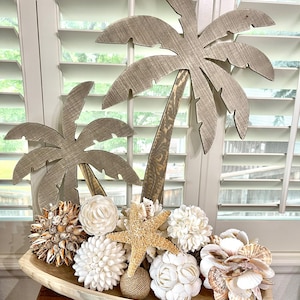 May include: A wooden bowl filled with various seashells, including starfish, and a decorative wooden palm tree cutout.