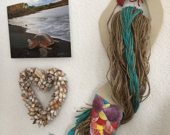 May include: A mermaid wall decor made of wood, yarn, and seashells. The mermaid has a turquoise tail, brown and blue yarn hair, and a seashell tail. A red lobster is attached to the top of the mermaid's head.