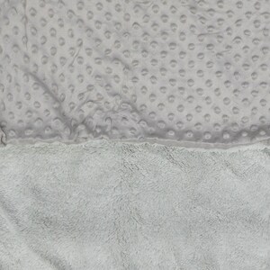 May include: A soft, grey blanket with a textured, dotted pattern on one side and a fluffy, plush texture on the other side.