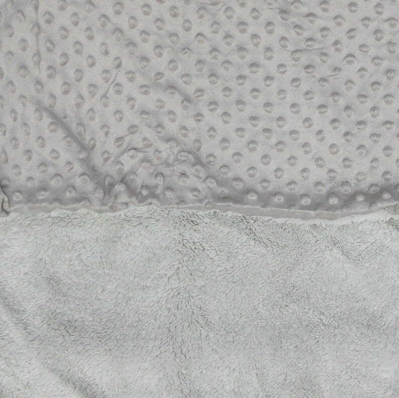 May include: A soft, grey blanket with a textured, dotted pattern on one side and a fluffy, plush texture on the other side.