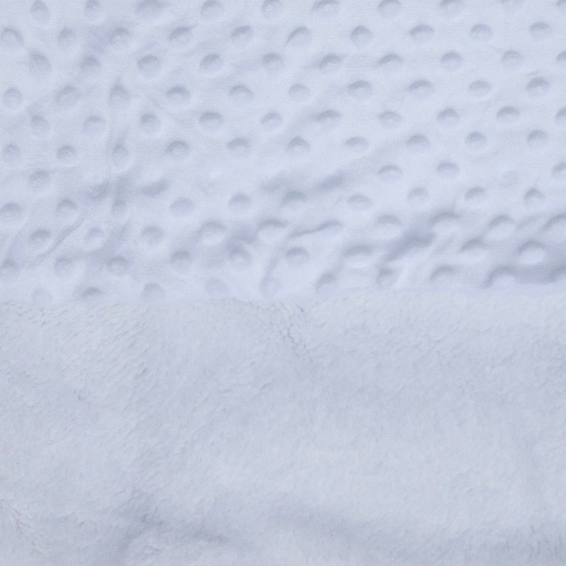 May include: A close-up of a white, plush blanket with a textured, dotted pattern. The blanket is soft and fluffy, and it appears to be made of a high-quality material.