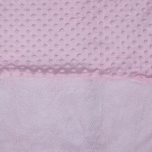 May include: A pink baby blanket with a soft, textured surface on one side and a smooth, plush surface on the other side.