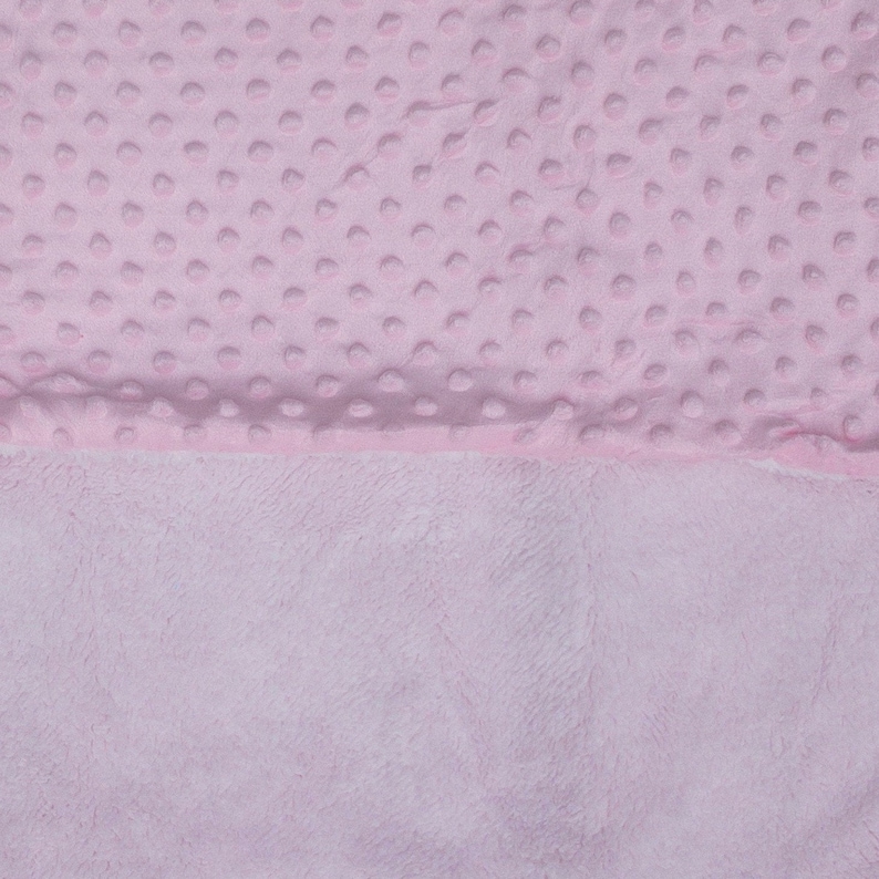 May include: A pink baby blanket with a soft, textured surface on one side and a smooth, plush surface on the other side.
