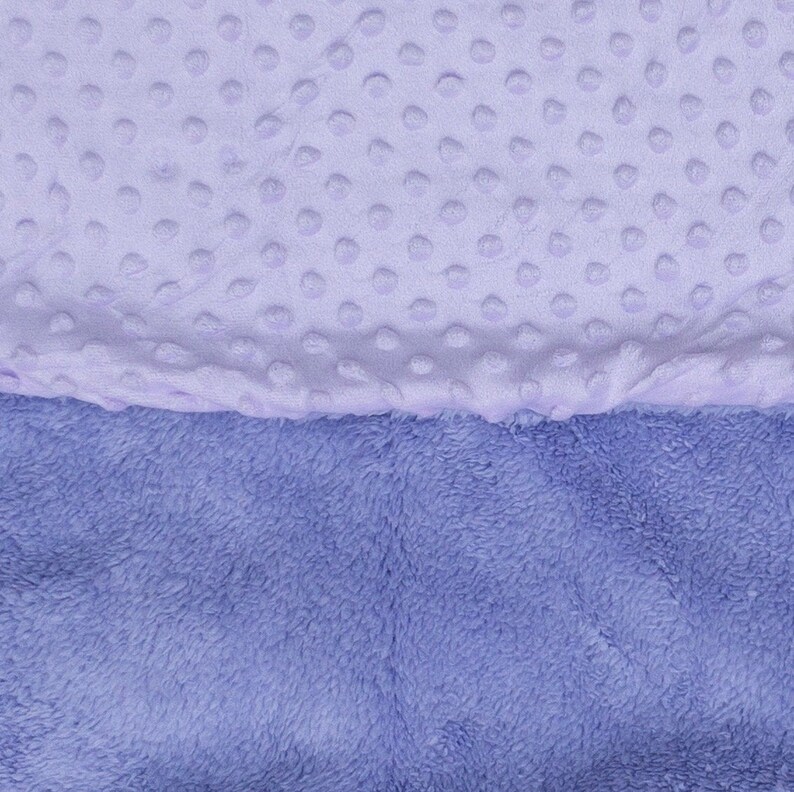 May include: A soft, two-toned baby blanket with a light purple side featuring a textured dot pattern and a darker purple side with a fuzzy texture.