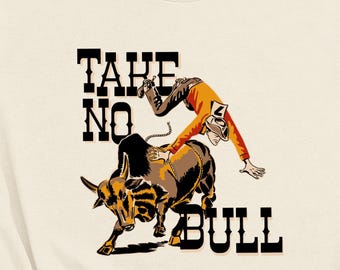 May include: A beige t-shirt with a graphic of a cowboy riding a bull. The text "Take No Bull" is printed on the shirt.