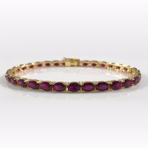 May include: A gold tennis bracelet with oval-shaped ruby red gemstones.
