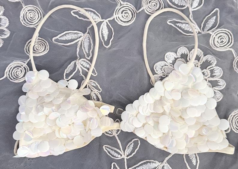 Puede incluir: Top de bikini blanco con lentejuelas y dise&ntilde;o halter. La parte superior est&aacute; cubierta de lentejuelas redondas e iridiscentes y tiene una base suave blanquecina. Las correas son finas y blancas. El top de bikini es una prenda de ba&ntilde;o.