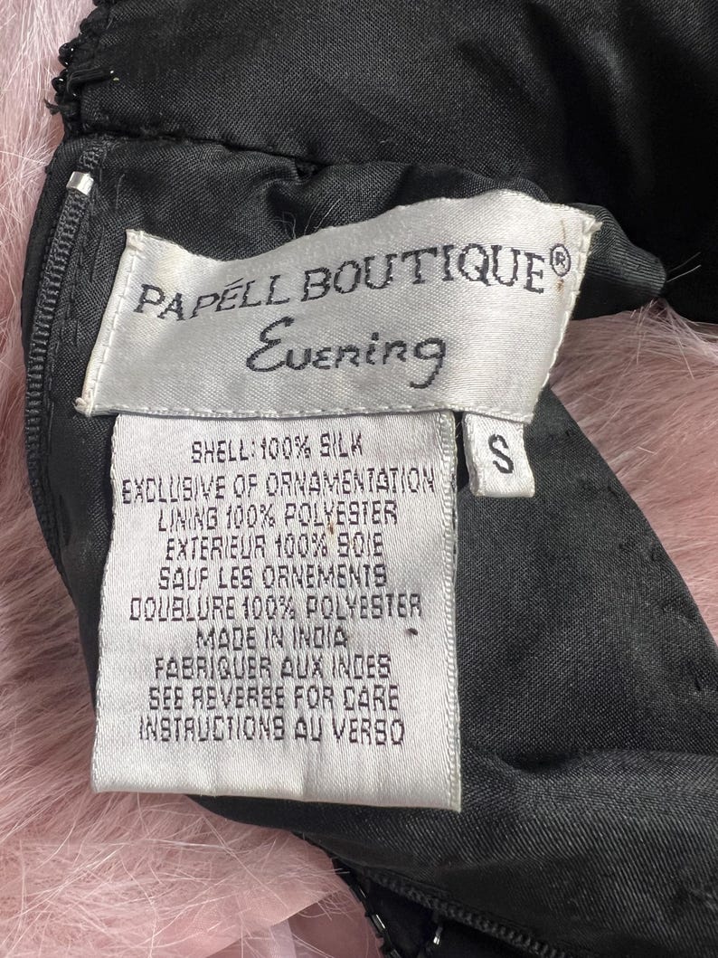 K&ouml;nnte beinhalten: Ein wei&szlig;es Etikett mit schwarzem Text, auf dem "PAPELL BOUTIQUE Evening" steht und die Stoffzusammensetzung des Kleidungsst&uuml;cks beschrieben wird. Das Etikett ist an einem schwarzen Kleidungsst&uuml;ck mit einem Rei&szlig;verschluss befestigt. Das Etikett lautet "SHELL: 100% SILK EXCLUSIVE OF ORNAMENTATION LINING 100% POLYESTER EXTERIEUR 100% SOIE SAUF LES ORNEMENTS DOUBLURE 100% POLYESTER MADE IN INDIA FABRIQUER AUX INDES SEE REVERSE FOR CARE INSTRUCTIONS AU VERSO" und hat ein Gr&ouml;&szlig;enetikett "S".