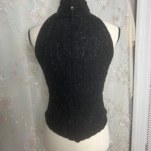 K&ouml;nnte beinhalten: Ein schwarzes, &auml;rmelloses Oberteil mit hohem Ausschnitt und einem geometrischen Muster aus Pailletten. Das Oberteil befindet sich auf einer wei&szlig;en Puppe.