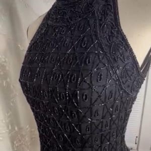 K&ouml;nnte beinhalten: Ein schwarzes Halstuch mit geometrischem Muster aus Pailletten. Das Oberteil ist &auml;rmellos und hat einen hohen Ausschnitt.