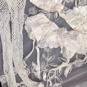 Puede incluir: Un surtido de lencer&iacute;a blanca, que incluye un sujetador adornado con lentejuelas iridiscentes, un sujetador de encaje y un par de medias de red. Los art&iacute;culos est&aacute;n dispuestos sobre una superficie gris con bordados florales.