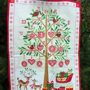 Puede incluir: Un calendario de adviento de tela blanca con forma de &aacute;rbol de Navidad con detalles rojos, verdes y dorados. El &aacute;rbol tiene 24 bolsillos numerados, cada uno con un dise&ntilde;o festivo diferente. Hay dos ciervos en la parte inferior del calendario y un trineo con regalos.