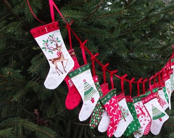 May include: A string of 12 Christmas stockings with red ribbon and different holiday designs, including reindeer, Christmas trees, and snowflakes. The stockings are numbered 1 through 12.