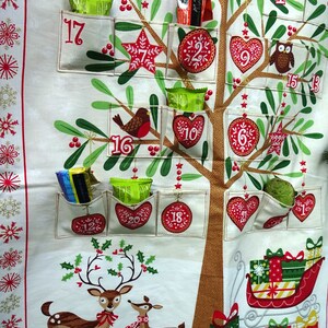 Puede incluir: Un calendario de adviento de tela blanca con forma de &aacute;rbol de Navidad con 24 bolsillos. Cada bolsillo tiene un n&uacute;mero del 1 al 24. Los bolsillos est&aacute;n llenos de peque&ntilde;os regalos y golosinas. Tambi&eacute;n hay p&aacute;jaros rojos, una estrella, un coraz&oacute;n, un b&uacute;ho y un reno en el calendario.