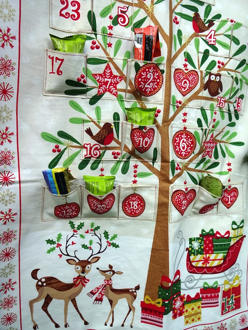 Puede incluir: Un calendario de adviento de tela blanca con forma de &aacute;rbol de Navidad con 24 bolsillos. Cada bolsillo tiene un n&uacute;mero del 1 al 24. Los bolsillos est&aacute;n llenos de peque&ntilde;os regalos y golosinas. Tambi&eacute;n hay p&aacute;jaros rojos, una estrella, un coraz&oacute;n, un b&uacute;ho y un reno en el calendario.