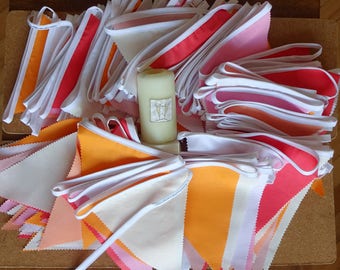 May include: A collection of fabric bunting flags in various shades of orange, pink, and white. The flags are folded and stacked, with a white candle in the center.
