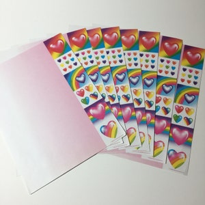 May include: A collection of heart-themed stickers with rainbow and pastel color schemes. The stickers feature large, glossy hearts, rainbows, and smaller heart designs. The stickers are arranged in strips and are next to a pink envelope.
