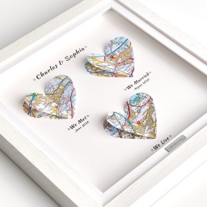 May include: A white frame with three paper map hearts. The hearts are folded to create a 3D effect. The text on the hearts reads "We Met June 2019", "We Married August 2020", and "We Live". The text at the top of the frame reads "Charles & Sophia".