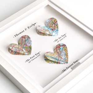 May include: A white frame with three paper map hearts. The hearts are folded to create a 3D effect. The text on the hearts reads "The First Day 22 February 2012", "The Yes Day 28 August 2016", and "The Forever Day". The names "Thomas & Evelyn" are written at the top of the frame.