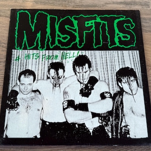May include: A square vinyl record cover featuring the band Misfits in bright green text at the top. Below, a black and white photograph shows four individuals with dark hair, some wearing armbands, with the text 4 HITS FROM HELL! in green.