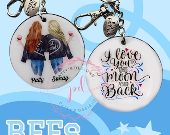May include: Two round keychains with a white background. One keychain features a cartoon illustration of two women with the text "Best Friends" and the names "Patty" and "Sandy". The other keychain features the text "I love you to the moon and back" with hearts and a moon.