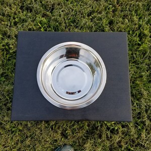 May include: A single circular stainless steel bowl set into a rectangular black base. The bowl features a polished, reflective metallic surface with a smooth, rounded rim, while the base is a solid, matte black platform with clean, straight edges.