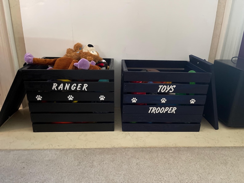 May include: Two black wooden slatted storage crates for pet items. The left crate features the white text RANGER and white paw prints. The right crate features the white text TOYS and TROOPER with white paw prints. Both crates are open.
