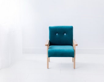 Un pequeño sillón infantil en tono turquesa intenso, un mini sillón de terciopelo para niño, un sillón tapizado suave con laterales de madera.