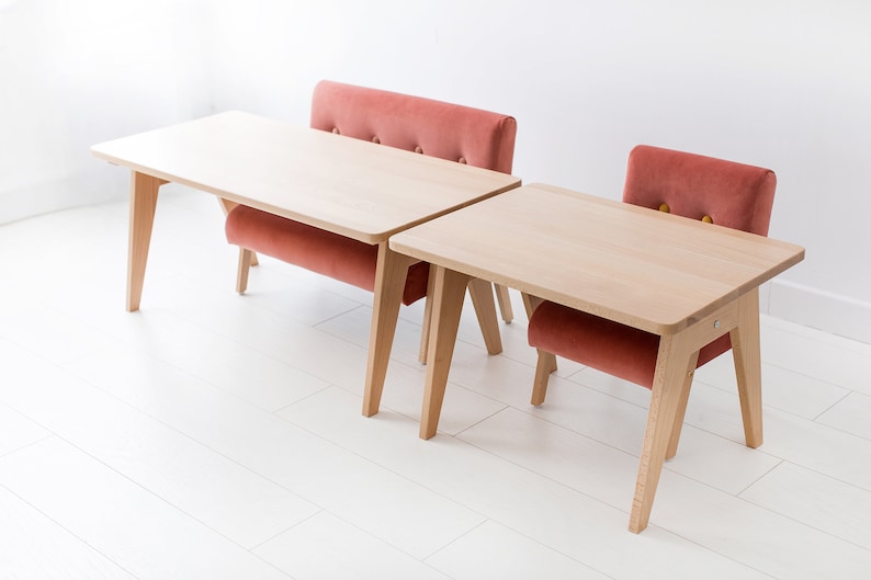 May include: A light wood table and bench set featuring a rectangular tabletop with rounded corners and angled legs. The bench has a tufted backrest upholstered in a dusty rose velvet fabric with visible button detailing and a matching seat cushion.