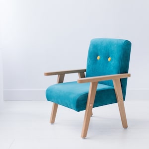 Peut inclure: Un fauteuil turquoise avec des accoudoirs et des pieds en bois. La chaise a un dossier et une assise rectangulaires avec deux boutons jaunes. Le cadre en bois a une finition naturelle. La chaise est pos&eacute;e sur un fond blanc.