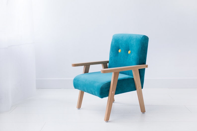 Peut inclure: Un fauteuil turquoise avec des accoudoirs et des pieds en bois. La chaise a un dossier et une assise rectangulaires avec deux boutons jaunes. Le cadre en bois a une finition naturelle. La chaise est pos&eacute;e sur un fond blanc.