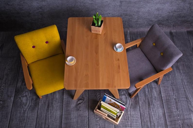 Peut inclure: Vue de dessus d'une petite table en bois avec deux fauteuils. Le fauteuil jaune a deux boutons violets, et le fauteuil gris a deux boutons jaunes. Deux tasses &agrave; th&eacute; et une petite plante sont sur la table.