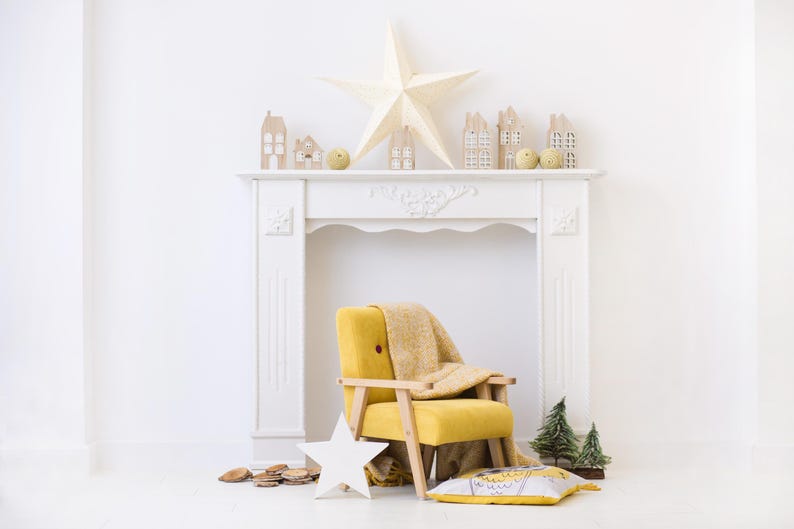 Peut inclure: Un manteau de chemin&eacute;e blanc avec des maisons en bois d&eacute;coratives, une grande &eacute;toile et de petits arbres verts. Un fauteuil jaune avec une couverture beige et un coussin en forme d'&eacute;toile sont devant. Une &eacute;toile en bois est au sol.