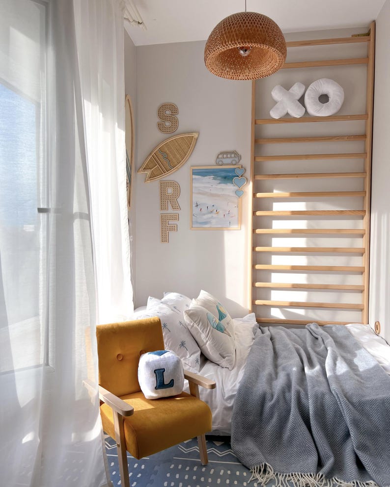 Peut inclure: Une chambre ensoleill&eacute;e sur le th&egrave;me c&ocirc;tier. Comprend un fauteuil jaune moutarde, un lit avec une couverture grise et des d&eacute;corations murales avec le mot "SURF". Un luminaire suspendu en osier est suspendu au plafond.