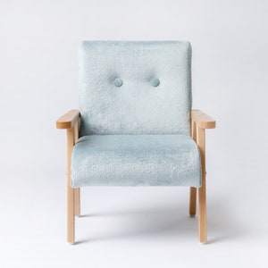 May include: A light blue upholstered armchair with light wood armrests and legs. The chair has a rectangular back with two button details. The chair is a light blue color and is set against a white background.