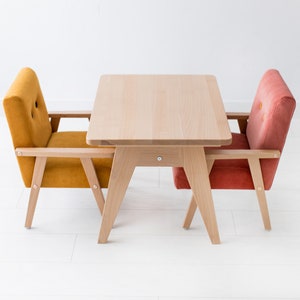 Peut inclure: Une petite table en bois clair avec deux fauteuils assortis. Un fauteuil est jaune moutarde, l'autre est orange rouge&acirc;tre. Les chaises et la table ont des cadres en bois clair, le tout sur fond blanc.