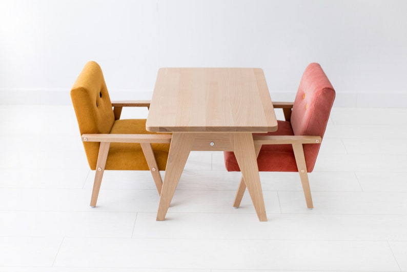 Peut inclure: Une petite table en bois clair avec deux fauteuils assortis. Un fauteuil est jaune moutarde, l'autre est orange rouge&acirc;tre. Les chaises et la table ont des cadres en bois clair, le tout sur fond blanc.