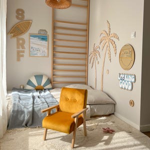 Peut inclure: Chambre d'enfant sur le th&egrave;me de la plage. Un fauteuil en velours orange avec des bras et des pieds en bois est pos&eacute; sur un tapis cr&egrave;me. D&eacute;corations murales : planche de surf, palmiers et l'expression "Looking Good".
