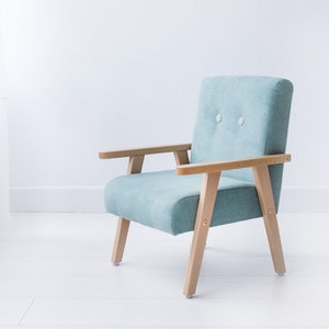 May include: A light blue armchair with wooden armrests and legs. The chair has a button-tufted back and a simple, modern design. The wooden frame is light-colored, and the chair is set against a white background.