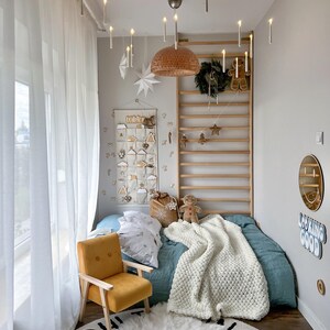 Peut inclure: Une chambre d&eacute;cor&eacute;e pour No&euml;l avec un lit bleu canard, une chaise moutarde et un tapis blanc duveteux. Des bougies d&eacute;coratives sont suspendues au plafond. Une &eacute;chelle en bois est orn&eacute;e de d&eacute;corations de No&euml;l.