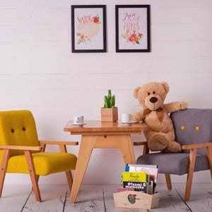 Peut inclure: Sc&egrave;ne de chambre d'enfant avec une petite table en bois, deux fauteuils et un ours en peluche. Le fauteuil jaune a deux boutons rouges. Le fauteuil gris a deux boutons jaunes. Deux tableaux encadr&eacute;s sont accroch&eacute;s au mur blanc.